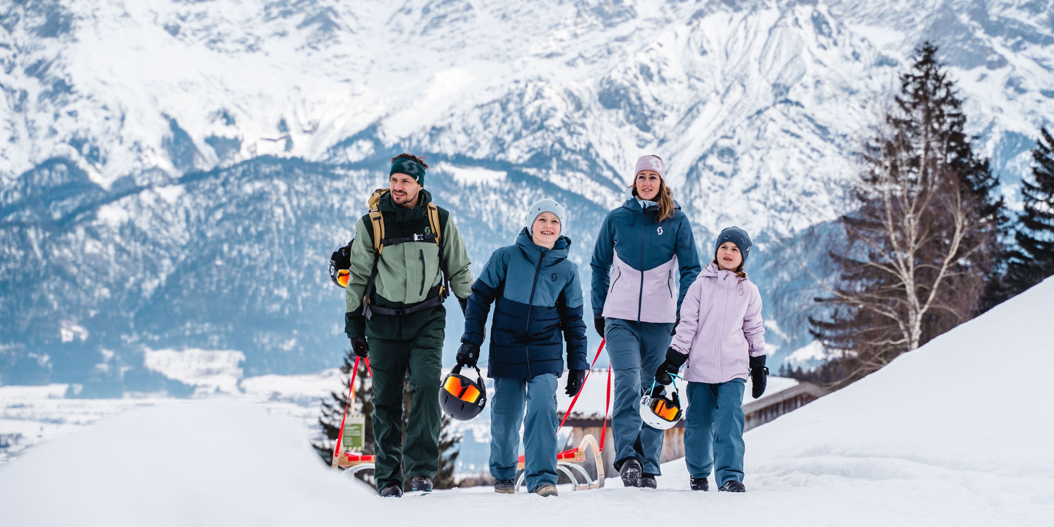 Familie mit Rodeln vor den verschneiten Leoganger Steinbergen